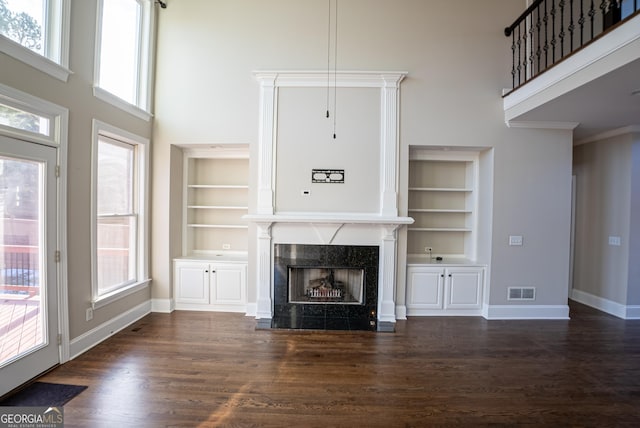 unfurnished living room with built in shelves, a fireplace, dark hardwood / wood-style flooring, and crown molding