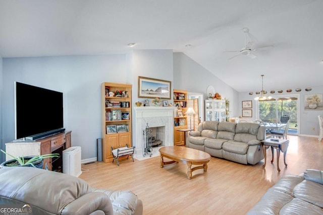 living room featuring ceiling fan with notable chandelier, vaulted ceiling, a premium fireplace, and light wood-type flooring