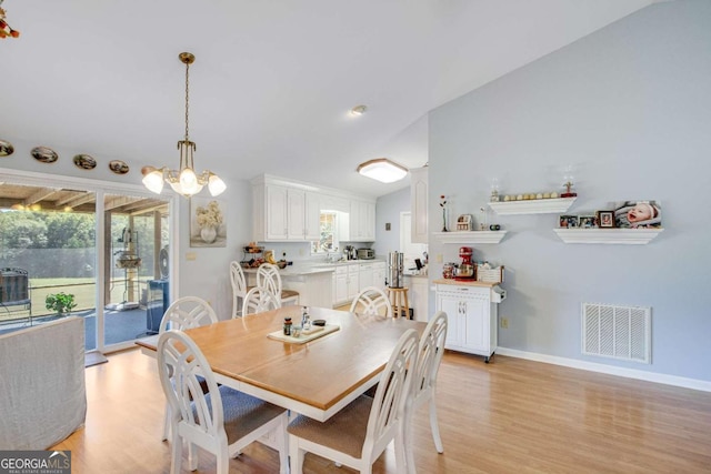 dining space with lofted ceiling, light wood-type flooring, and an inviting chandelier