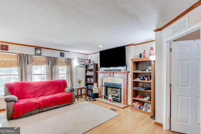 living room featuring a tile fireplace, crown molding, a textured ceiling, and hardwood / wood-style flooring