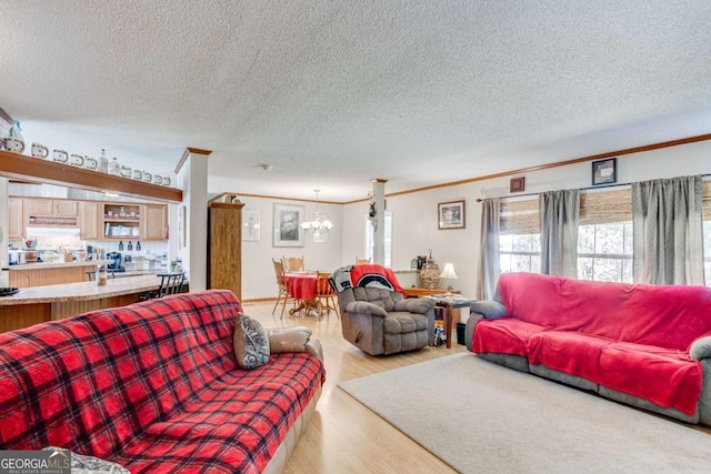 living room featuring a textured ceiling, an inviting chandelier, ornamental molding, and light wood-type flooring