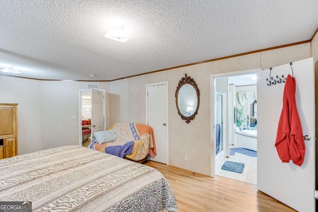 bedroom with a textured ceiling, ensuite bathroom, crown molding, and hardwood / wood-style floors