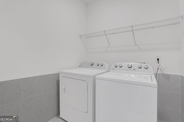 clothes washing area featuring washer and clothes dryer and tile walls