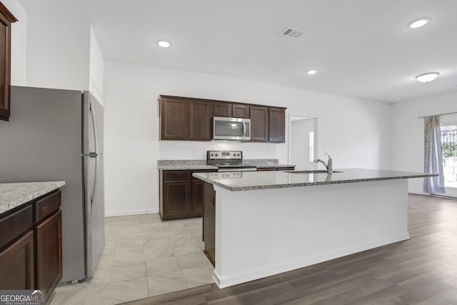 kitchen with a kitchen island with sink, sink, light stone counters, and appliances with stainless steel finishes