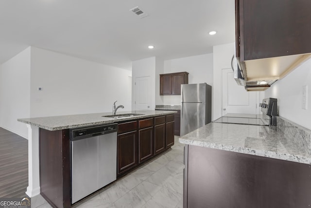 kitchen featuring appliances with stainless steel finishes, sink, light stone counters, dark brown cabinets, and a center island with sink