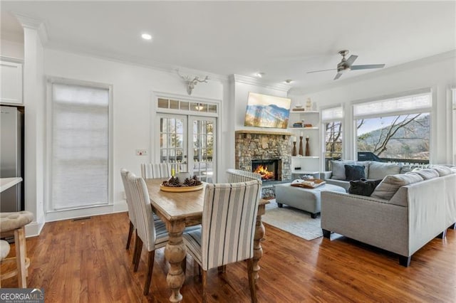 dining space with ceiling fan, a fireplace, french doors, wood-type flooring, and ornamental molding