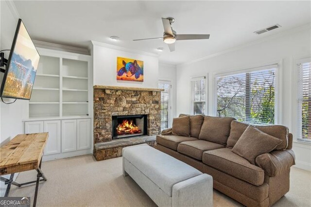 living room with ceiling fan, light colored carpet, a stone fireplace, and ornamental molding