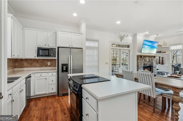 kitchen featuring black appliances, white cabinets, backsplash, and a fireplace