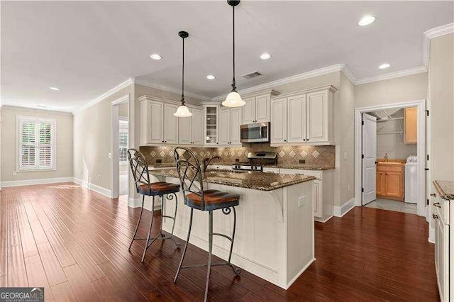 kitchen with washer / dryer, stainless steel appliances, dark stone counters, and a kitchen island