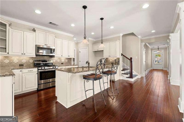 kitchen with dark wood-type flooring, a center island with sink, stainless steel appliances, and dark stone countertops