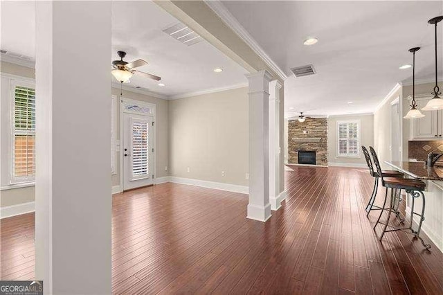 unfurnished living room featuring decorative columns, a stone fireplace, crown molding, and ceiling fan