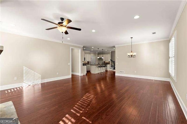 unfurnished living room featuring ceiling fan with notable chandelier, dark hardwood / wood-style flooring, and crown molding