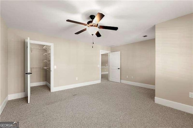 unfurnished bedroom with ceiling fan, a closet, a spacious closet, and carpet floors