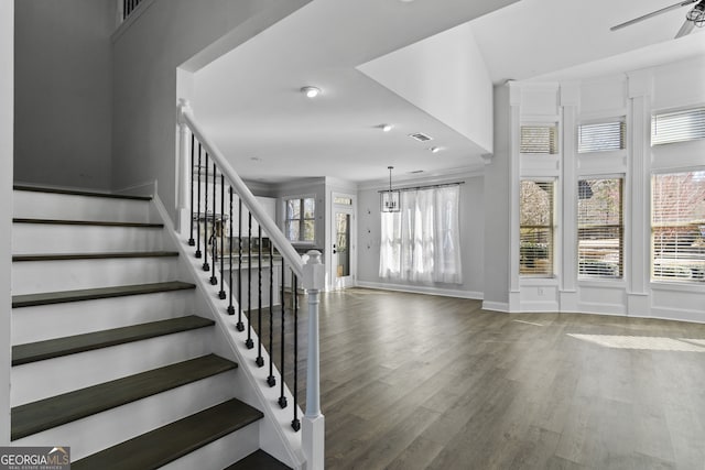 stairway with ornamental molding, ceiling fan with notable chandelier, and hardwood / wood-style floors