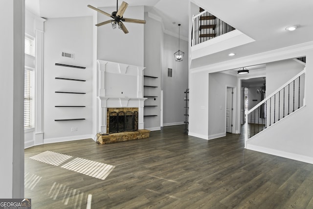 unfurnished living room featuring a stone fireplace, ceiling fan, dark hardwood / wood-style floors, a high ceiling, and ornamental molding