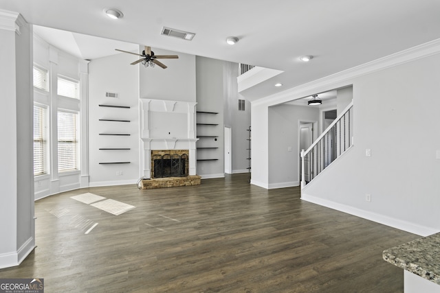 unfurnished living room with built in shelves, dark hardwood / wood-style flooring, a stone fireplace, ornamental molding, and ceiling fan