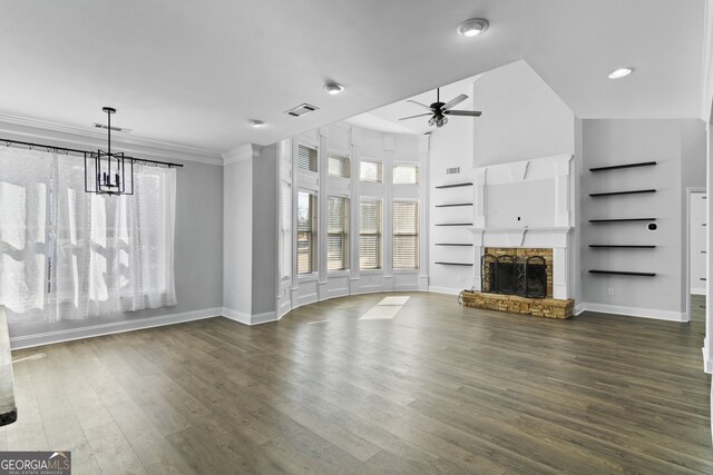 unfurnished living room with dark wood-type flooring, ornamental molding, ceiling fan with notable chandelier, and a stone fireplace