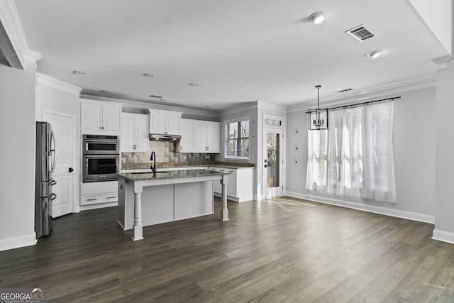 kitchen featuring appliances with stainless steel finishes, white cabinetry, dark stone counters, decorative backsplash, and a kitchen island with sink