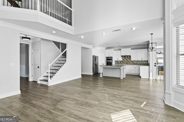 unfurnished living room featuring dark hardwood / wood-style floors, ornamental molding, and a towering ceiling