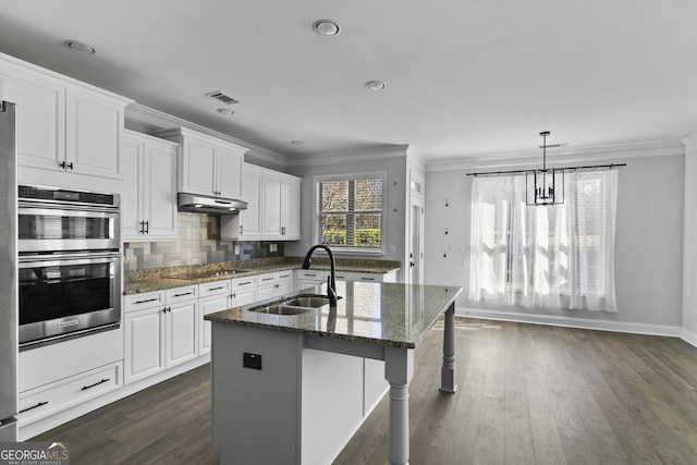 kitchen featuring an island with sink, tasteful backsplash, dark stone counters, white cabinets, and sink