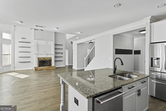 kitchen with white cabinetry, a center island with sink, a stone fireplace, appliances with stainless steel finishes, and sink