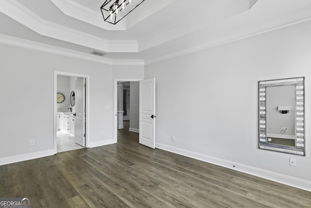 unfurnished bedroom featuring dark wood-type flooring, an inviting chandelier, ornamental molding, a raised ceiling, and ensuite bathroom