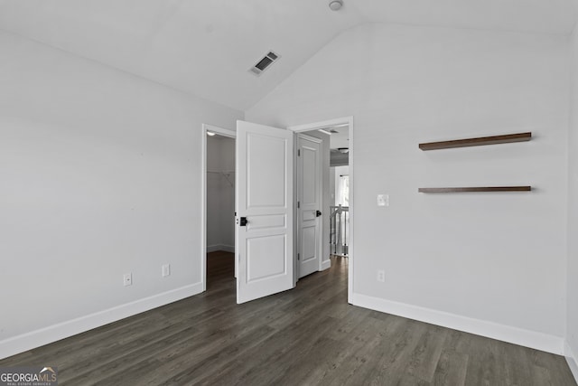 unfurnished bedroom with a closet, a walk in closet, dark hardwood / wood-style floors, and lofted ceiling