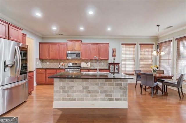 kitchen featuring decorative light fixtures, a kitchen island with sink, appliances with stainless steel finishes, and sink