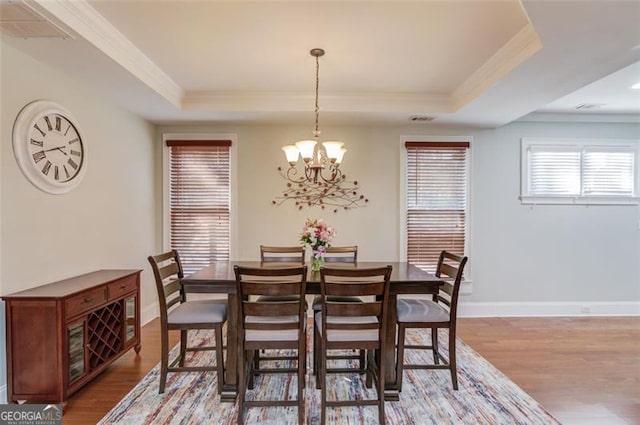 dining space featuring a raised ceiling, ornamental molding, a chandelier, and light hardwood / wood-style floors