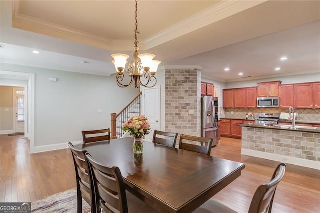 dining room featuring an inviting chandelier, sink, a tray ceiling, light hardwood / wood-style flooring, and crown molding