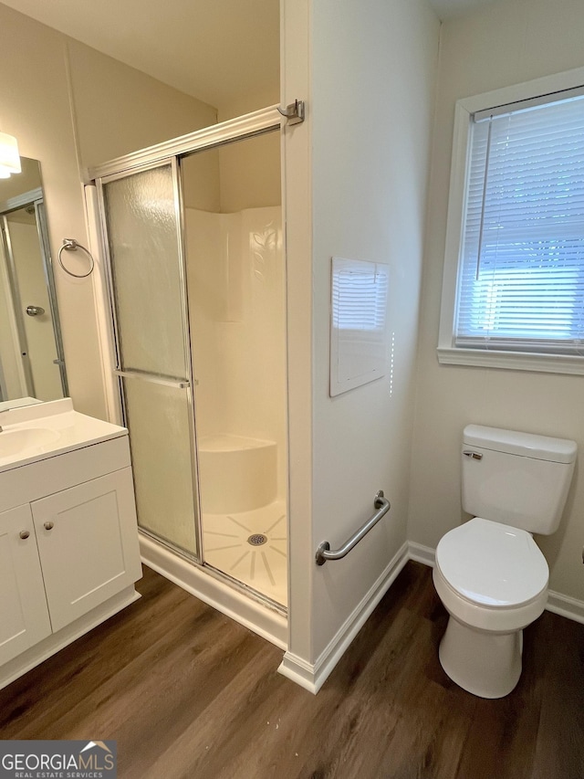 bathroom with toilet, a shower with shower door, hardwood / wood-style floors, and vanity