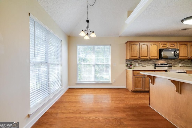 kitchen featuring decorative light fixtures, backsplash, a notable chandelier, vaulted ceiling, and stainless steel electric range oven