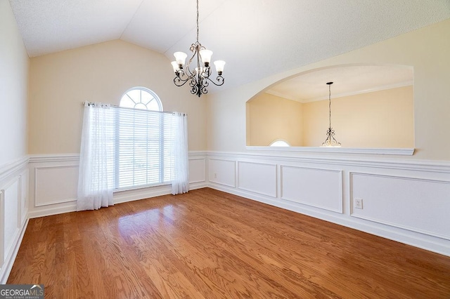 empty room with hardwood / wood-style floors, lofted ceiling, and an inviting chandelier