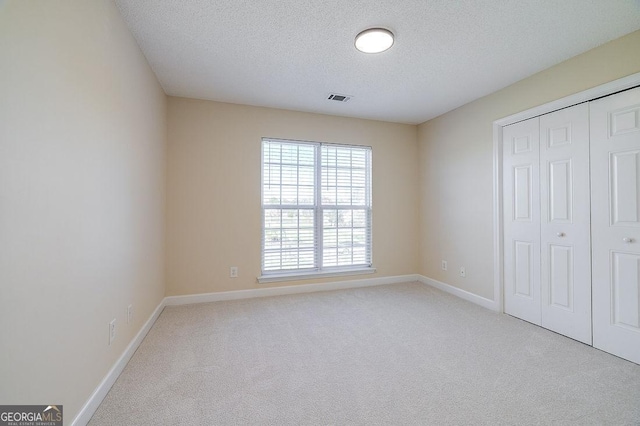 unfurnished bedroom with light carpet, a closet, and a textured ceiling