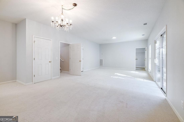 carpeted empty room with a textured ceiling and a chandelier