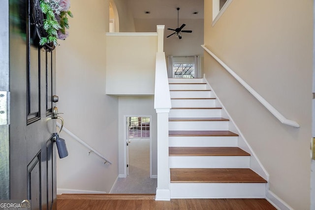 stairs featuring ceiling fan, a healthy amount of sunlight, a towering ceiling, and hardwood / wood-style flooring