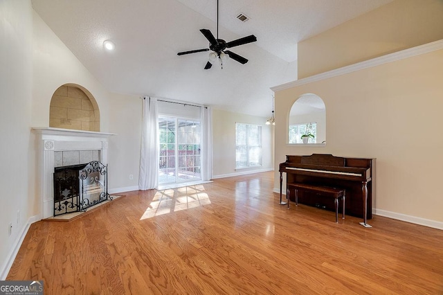 living room with ceiling fan, light hardwood / wood-style flooring, high vaulted ceiling, and a tiled fireplace