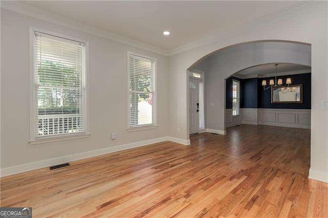 empty room with hardwood / wood-style floors, ornamental molding, and a chandelier