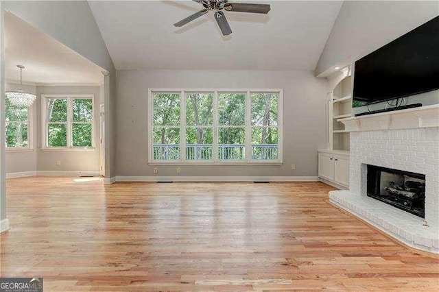 unfurnished living room featuring a fireplace, vaulted ceiling, ceiling fan with notable chandelier, light hardwood / wood-style flooring, and built in shelves