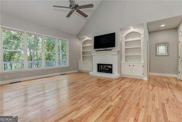 unfurnished living room with a brick fireplace, ceiling fan, light wood-type flooring, high vaulted ceiling, and built in shelves