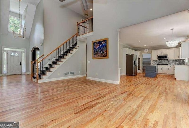 unfurnished living room featuring sink, a towering ceiling, and light wood-type flooring