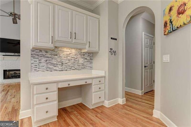 interior space with ceiling fan, a fireplace, ornamental molding, built in desk, and light hardwood / wood-style flooring