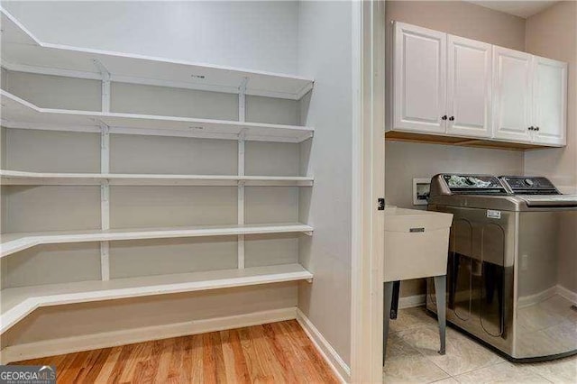 clothes washing area featuring light hardwood / wood-style flooring, washing machine and dryer, and cabinets