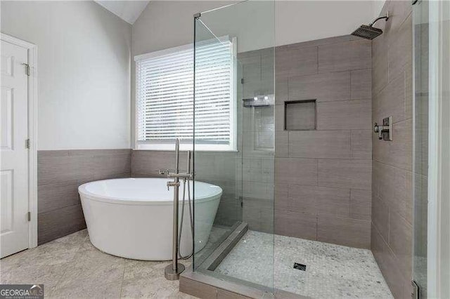 bathroom with vaulted ceiling, tile patterned flooring, tile walls, and separate shower and tub