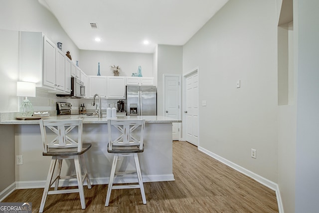 kitchen with a kitchen bar, light hardwood / wood-style floors, appliances with stainless steel finishes, decorative backsplash, and white cabinets