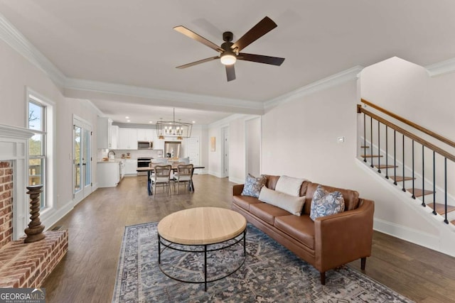 living room featuring ceiling fan with notable chandelier, dark hardwood / wood-style flooring, a fireplace, sink, and crown molding