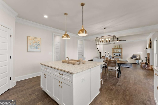 kitchen with a brick fireplace, a center island, crown molding, white cabinetry, and hanging light fixtures