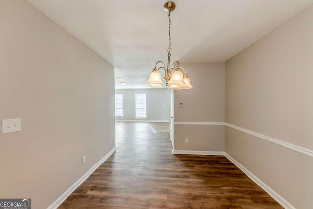 unfurnished dining area featuring a textured ceiling, a chandelier, and dark hardwood / wood-style floors