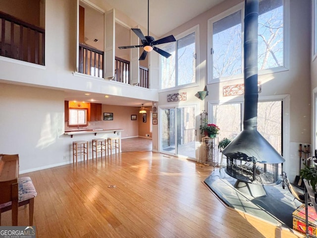 living room with a high ceiling, a wood stove, ceiling fan, and light wood-type flooring