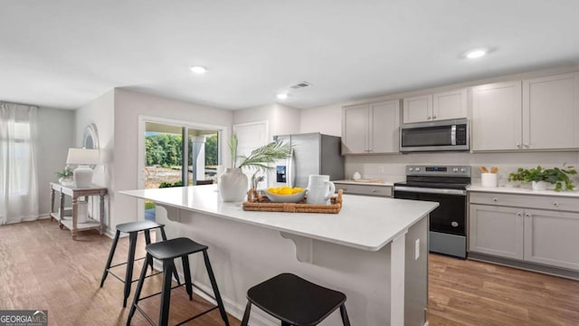 kitchen with light wood-type flooring, stainless steel appliances, a breakfast bar, and a center island